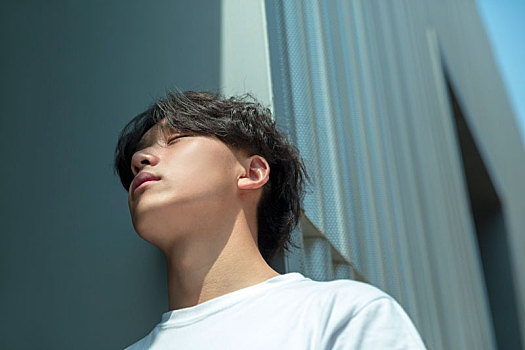 一名眯着眼睛休息的亚裔男孩在天台靠着休息