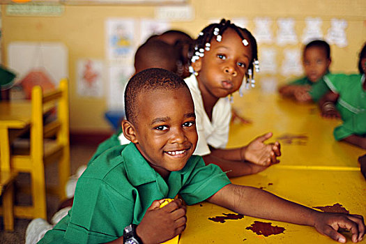 dominica,roseau,preschool,social,center,smiling,boy,at,yellow,school,table