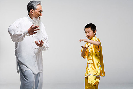 一位老者正在教一个小男孩练太极