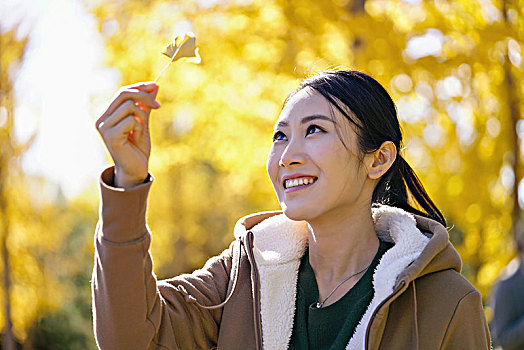 快乐的年轻女子手拿银杏叶