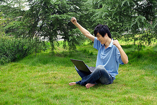 盘腿坐在草地上使用电脑的年轻男人