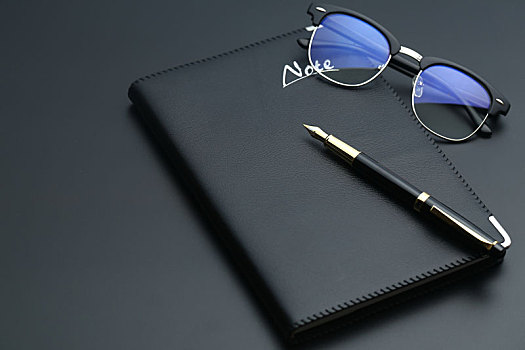 金笔,眼镜,计算器和笔记本放在黑色桌面上