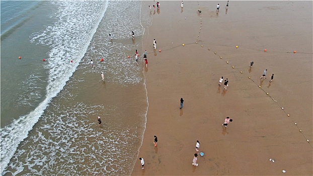 山东省日照市,清晨里的海水浴场少了人头攒动,游客悠闲漫步沙滩感受清凉