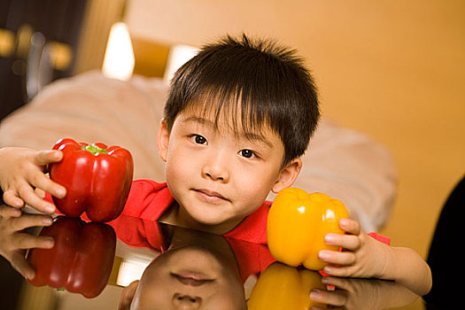 坐在桌边拿着蔬菜的小男孩对着镜头做表情
