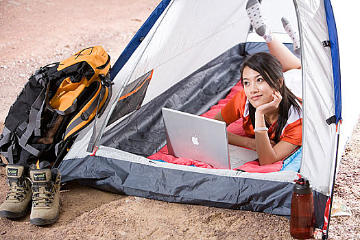 一个年轻的女孩在郊外的帐蓬里面玩电脑