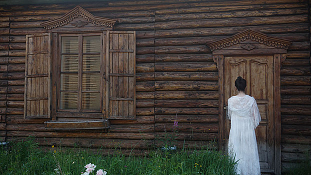 一个穿白色长裙的女孩在木屋门前开门