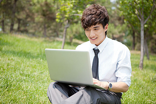 坐在草坪上看电脑的男青年