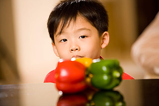 坐在桌边拿着蔬菜的小男孩对着镜头做表情