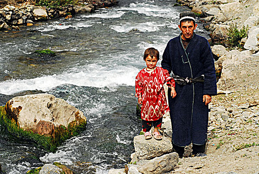 tajikistan,penjakent,father,and,child,in,traditional,dress,walking,by,the,river