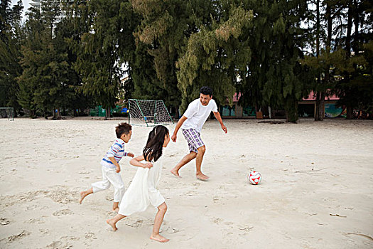 中年人和小女孩,小男孩在海边踢足球