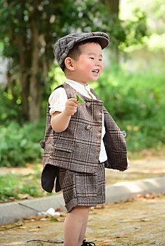 阳光下林荫小路上穿着短袖西服手拿树叶玩耍的小男孩