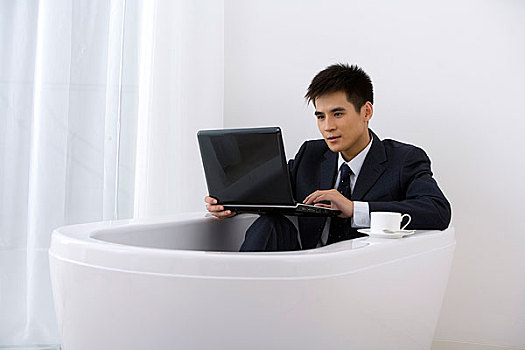 一个穿职业装的男人拿着电脑在浴缸里