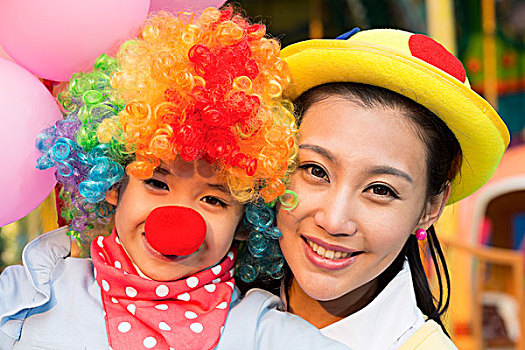 小女孩扮小丑和年轻妈妈在游乐园