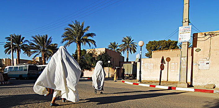 algeria,ben,isguen,people,walking,on,street,with,blue,sky,and,palm,trees,in,the,background