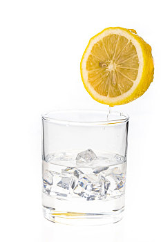 一个新鲜的切开的柠檬正从空中往一个盛有冰块的玻璃水杯滴水