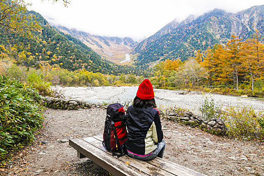 一个手拿登山杖坐在秋天山谷河边的女性徒步旅行者