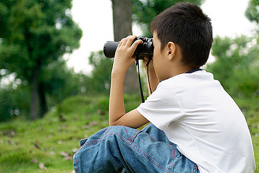 坐在草地上用望远镜看着前方的小男孩