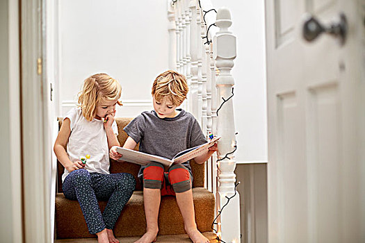 两个孩子,坐,并排,楼梯,在家,读,书本,一起