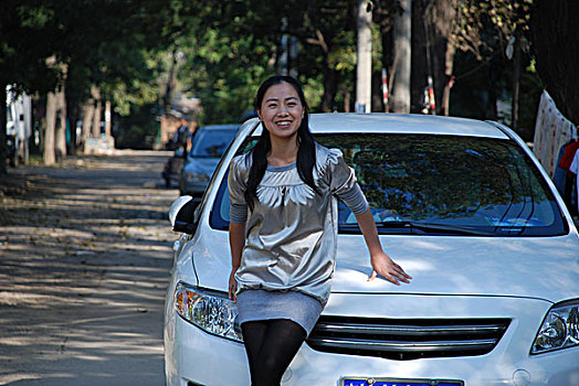 一名年轻女性微笑着依靠在汽车前