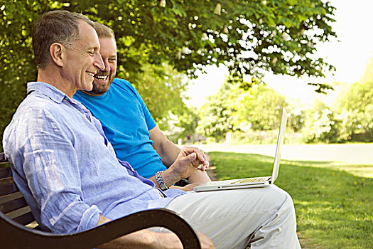 两个男人,坐,公园长椅,使用笔记本,微笑