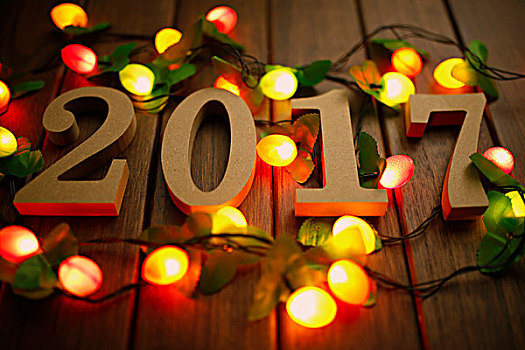 2017新年快乐,木质数字和闪烁的彩灯放在复古桌面上