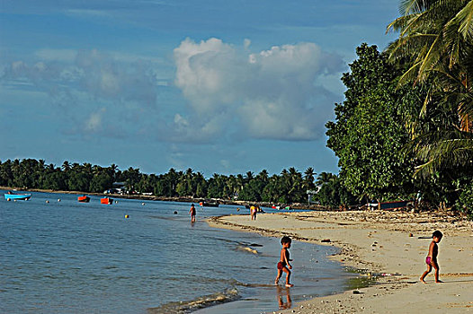 tuvalu,funafuti,boats,in,blue,sea,with,children,standing,on,pier,by,coastline,palm,trees,against,sky