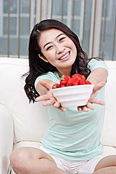 年轻女士坐在沙发上拿着一碗草莓