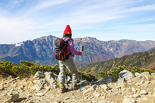 一个手拿登山杖站在山顶看着远方风景的女性徒步旅行者背影