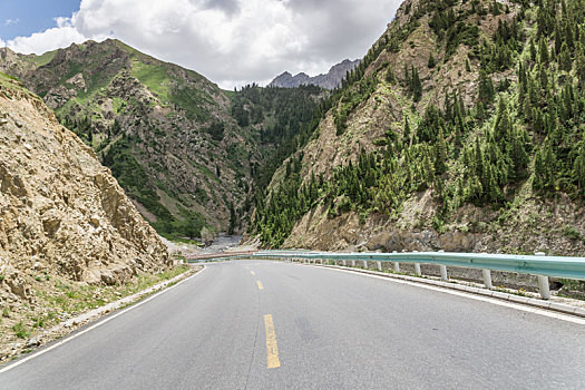 中国新疆夏季蓝天白云下高山森林g217独库公路直行道正面