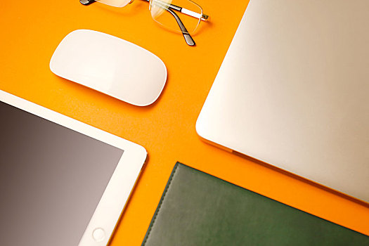 书,鼠标,电脑等办公用品陈列在橙色背景的桌面上