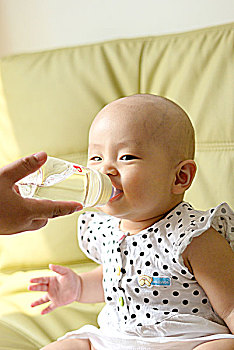 坐在沙发上用奶瓶喝水的婴儿