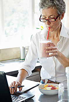 女人喝冰沙,在笔记本电脑打字