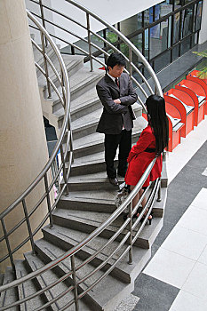 一对年轻男女站在办公楼的楼梯上聊天