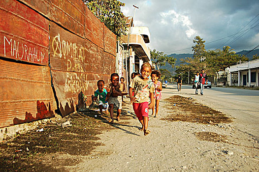 group,of,timorese,children,running,in,the,street,under,dark,clouds,with,a,blond,boy,middle