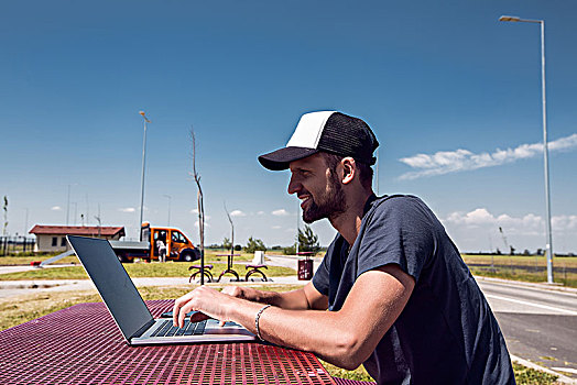 男人,棒球帽,坐,路边,野餐桌,打字,笔记本电脑