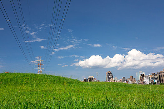 堤防公园绿草岥上的电塔,蓝天白云下的城市