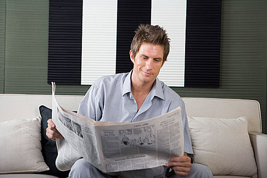 一个穿着休闲装的男人坐在沙发上看报