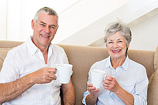 老年,夫妻,坐,沙发,喝咖啡,看镜头,微笑