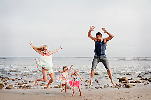 父母,两个女孩,跳跃,半空,海滩