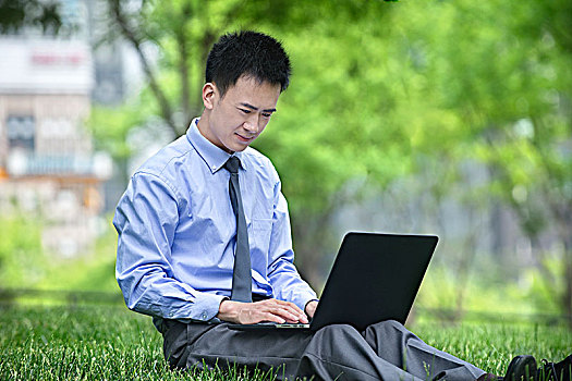 坐在草地上拿电脑的商务男士
