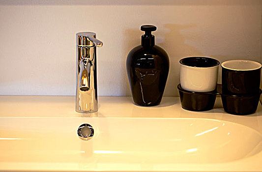卫生间水池边摆放着黑的陶瓷瓶子和杯子