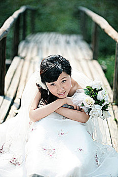 手持玫瑰花坐在木桥上穿婚纱的女子
