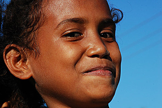 portrait,of,a,timorese,girl,with,curly,hair,closing,her,eyes,because,the,sun