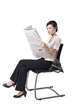 坐在椅子上看英文报纸的商务女性