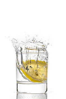 一片新鲜的柠檬片掉入玻璃水杯中的瞬间,水花正要从杯里飞溅而出