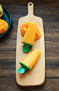 用芒果果泥制作的芒果雪糕和新鲜切好的芒果摆放在木桌上
