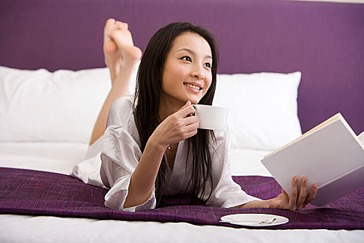 一个女人趴在床上边看书边喝咖啡