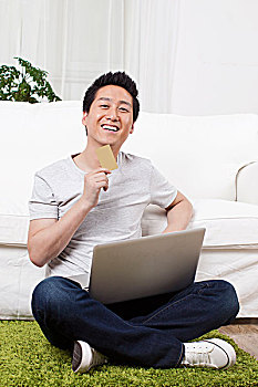 一个坐在绿色地毯上用笔记本电脑的青年男士
