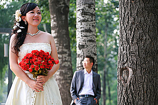 树林中手捧玫瑰花的新娘与新郎