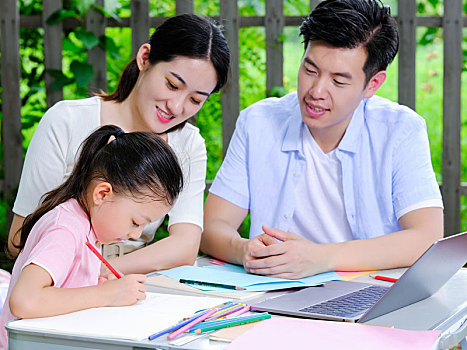 年轻的父母在户外辅导孩子写作业